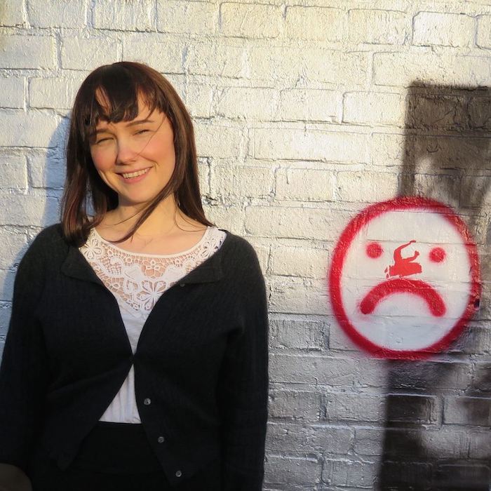 Photograph of me standing next to a frowny face on a painted wall