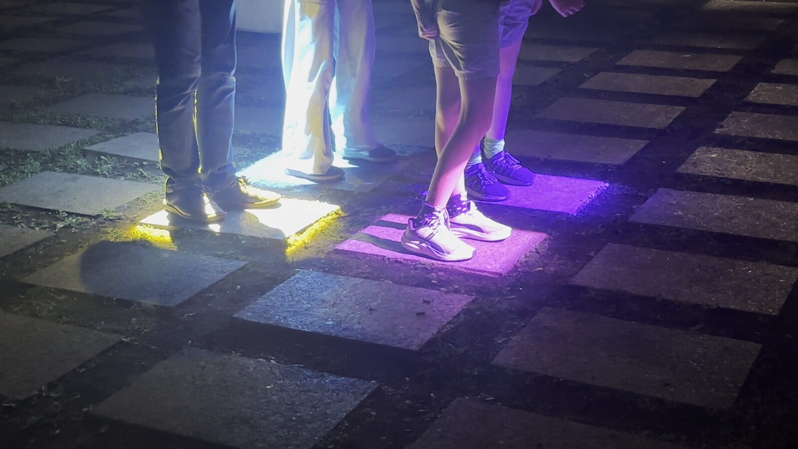 Des pieds, de près, posés sur des dalles éclairées de jaune et de violet.