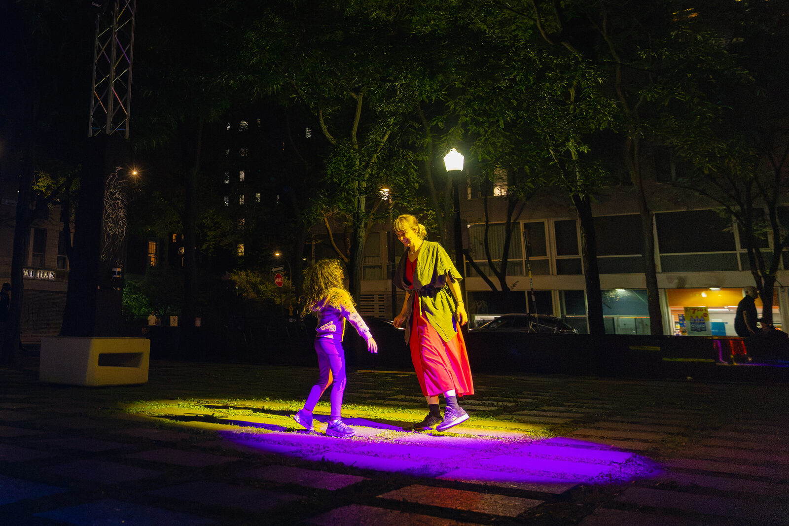 Deux personnes dansent ensemble dans des flaques de lumière violette et jaune, le soir, dans un parc.