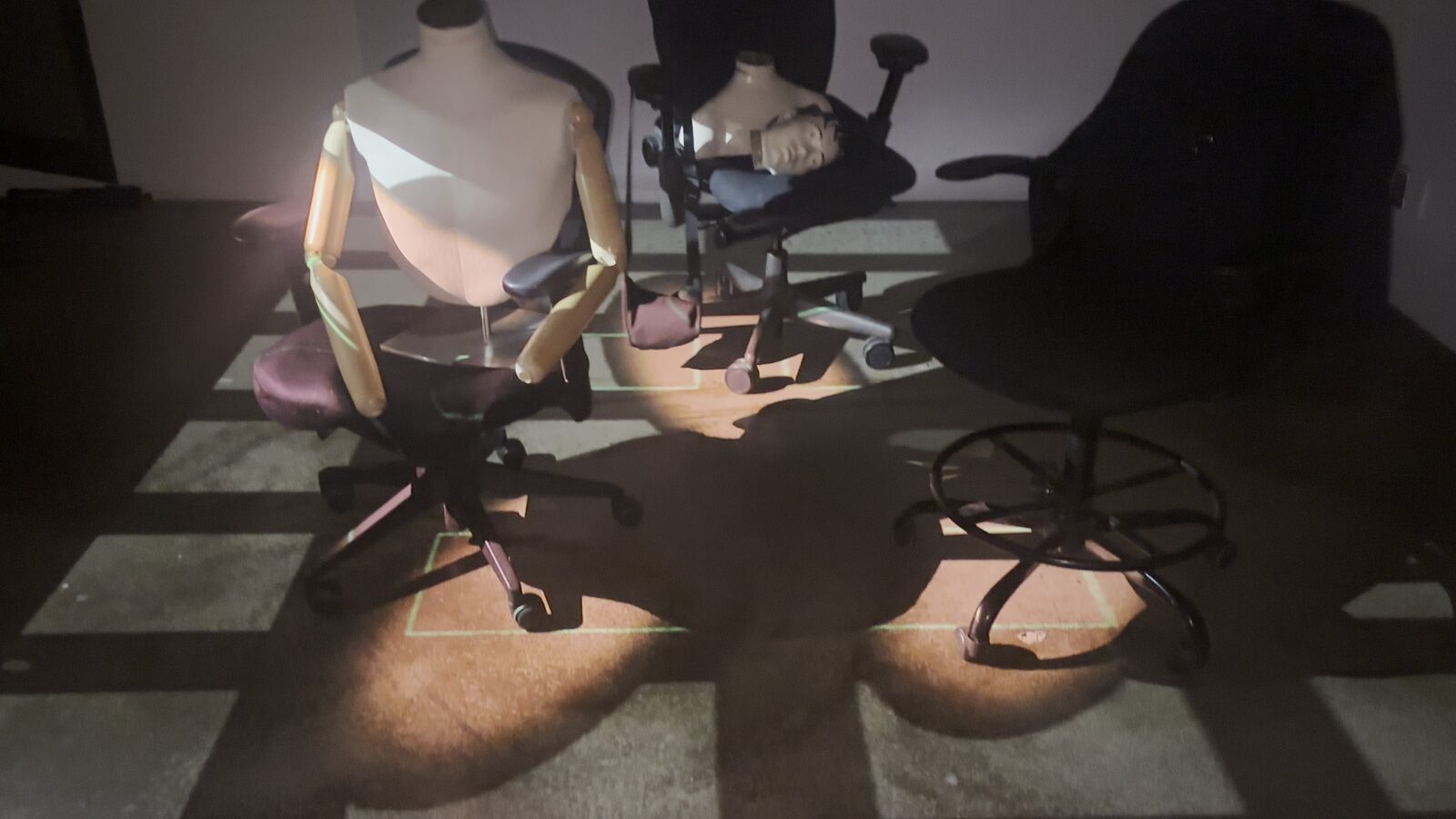 Des mannequins posés sur des chaises de bureau, éclairés par la lumière projetée, en atelier.
