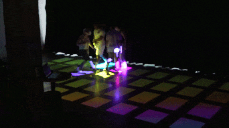 Several players standing on a colourful projected light grid on the floor