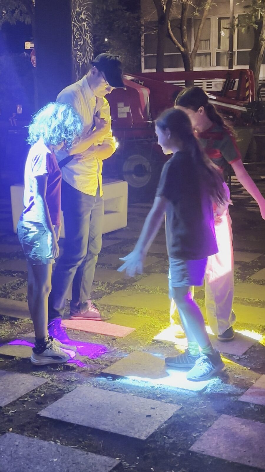 Un groupe de personnes se tient tout près, baigné de lumière bleue, sur les dalles du parc.