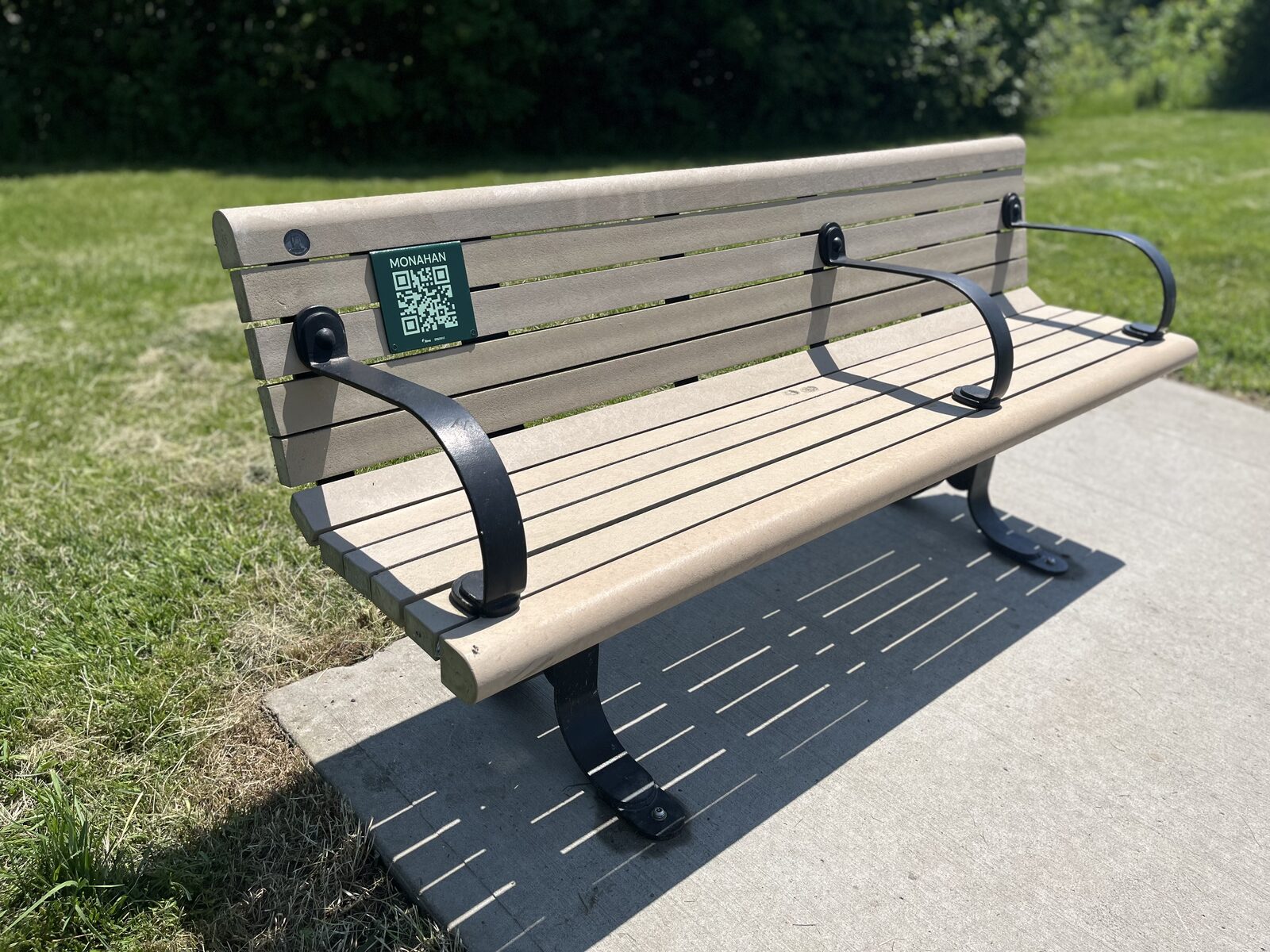 Une petite plaque à code QR fixée sur le dossier d'un banc, le long du sentier.