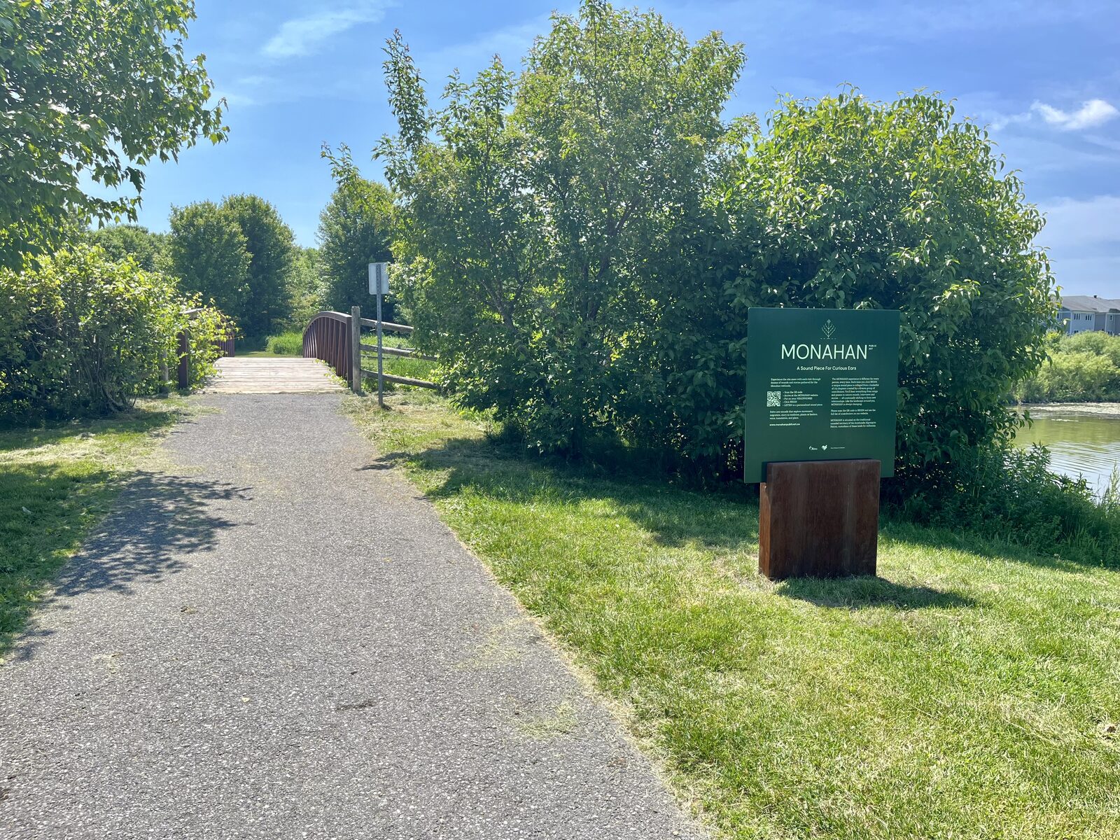 Le panneau MONAHAN au bord du sentier, avec l'eau du marais et les arbres derrière.