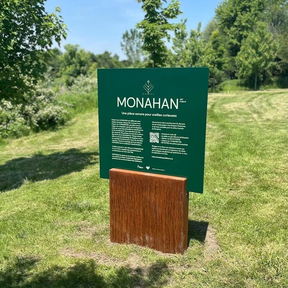 Un panneau vert « MONAHAN » portant un code QR, planté dans l'herbe au bord du marais.