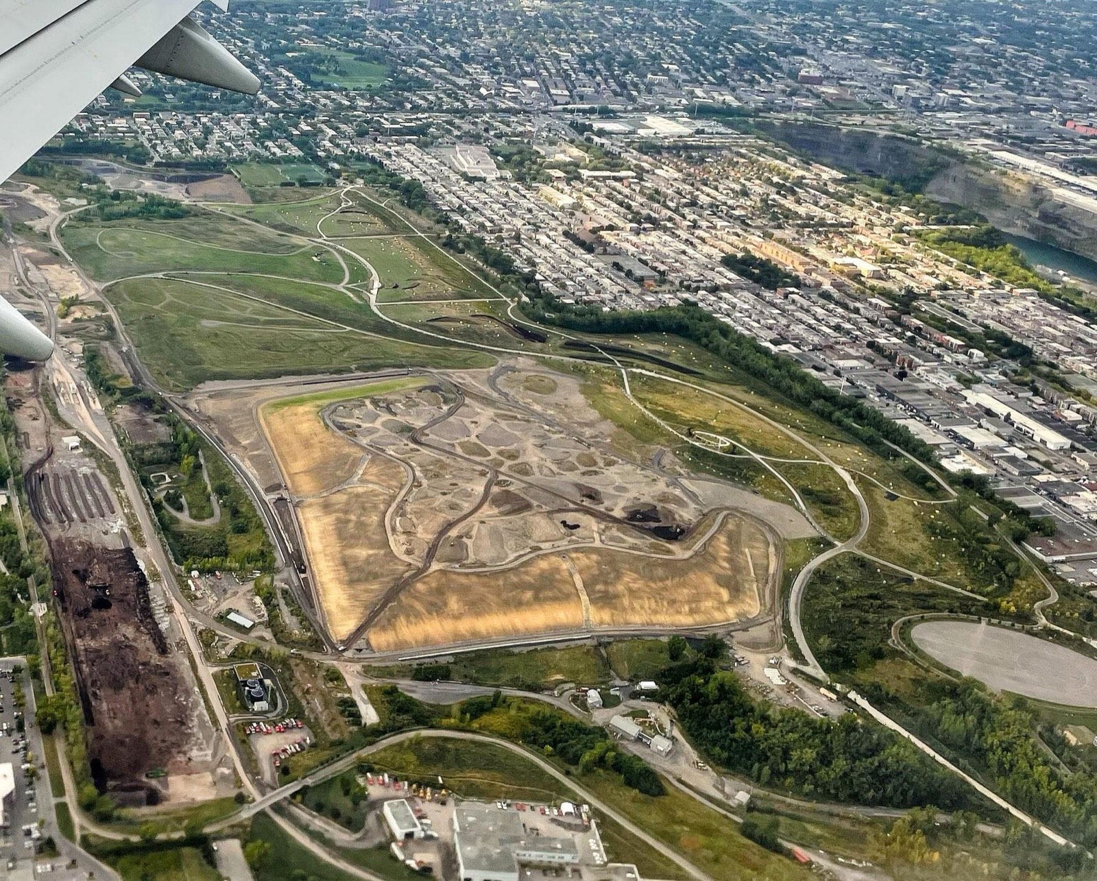 Vue aérienne du parc Frédéric-Back l'été : de grandes collines vertes, d'anciennes zones d'enfouissement, une carrière et le quartier tout autour.