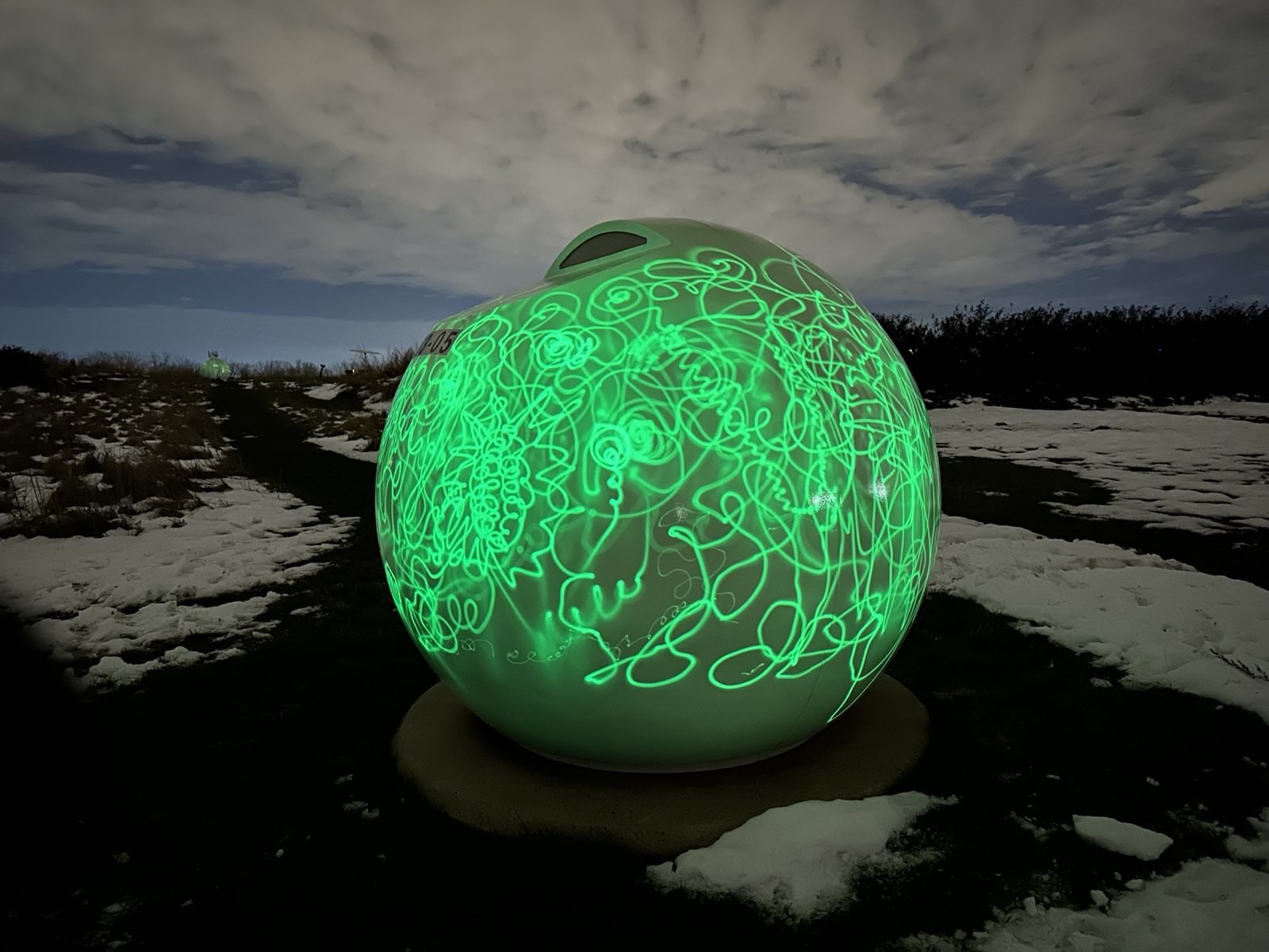 Une grande orbe verte qui brille dans la neige, au crépuscule, entièrement couverte de dessins de lumière tracés à la main.