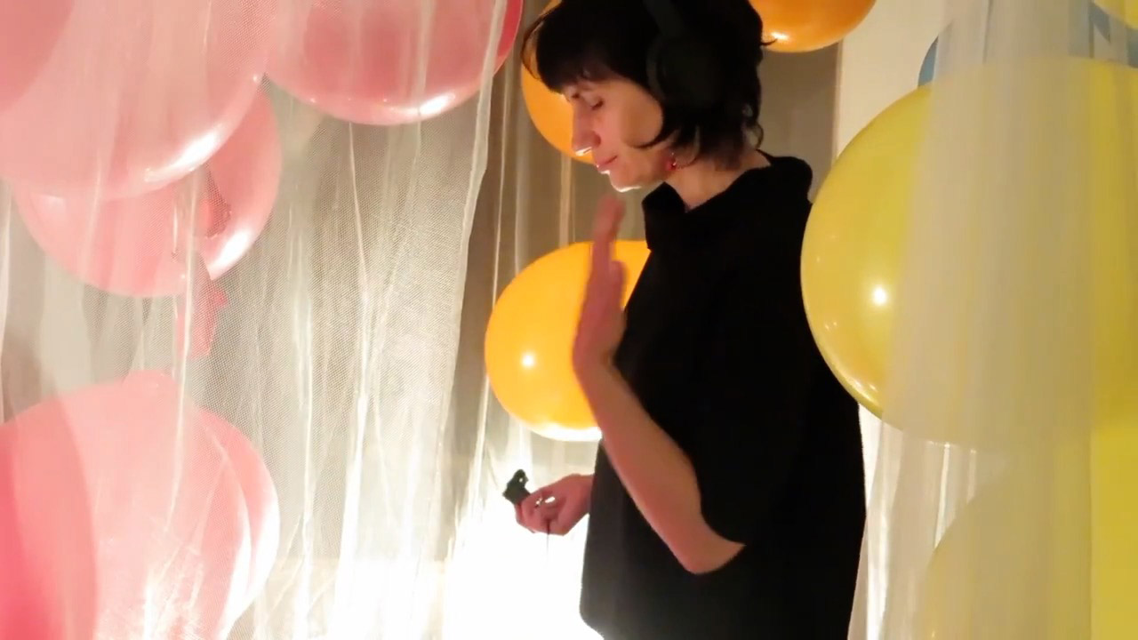 A person standing in between pink and yellow balloons wafting a scent towards their face